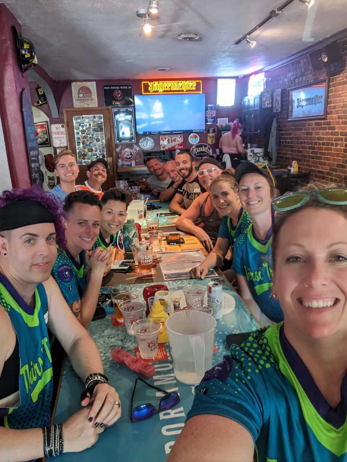 Group of people in colorful jerseys smiling and posing together at a restaurant table.