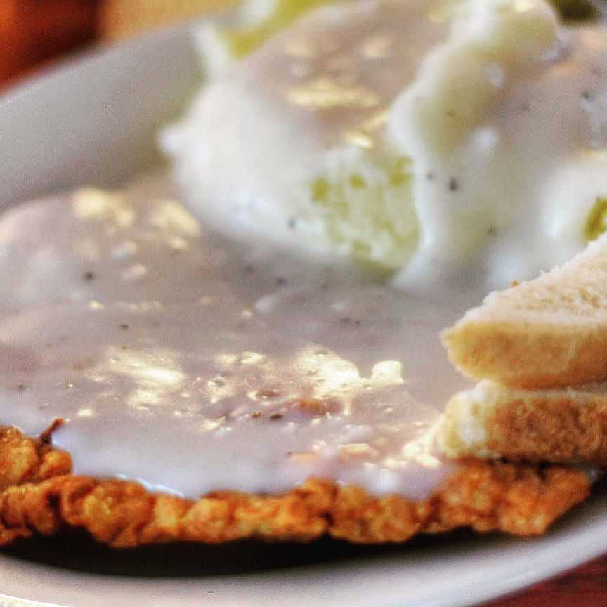 Chicken fried steak with gravy, mashed potatoes, and toast on a white plate.