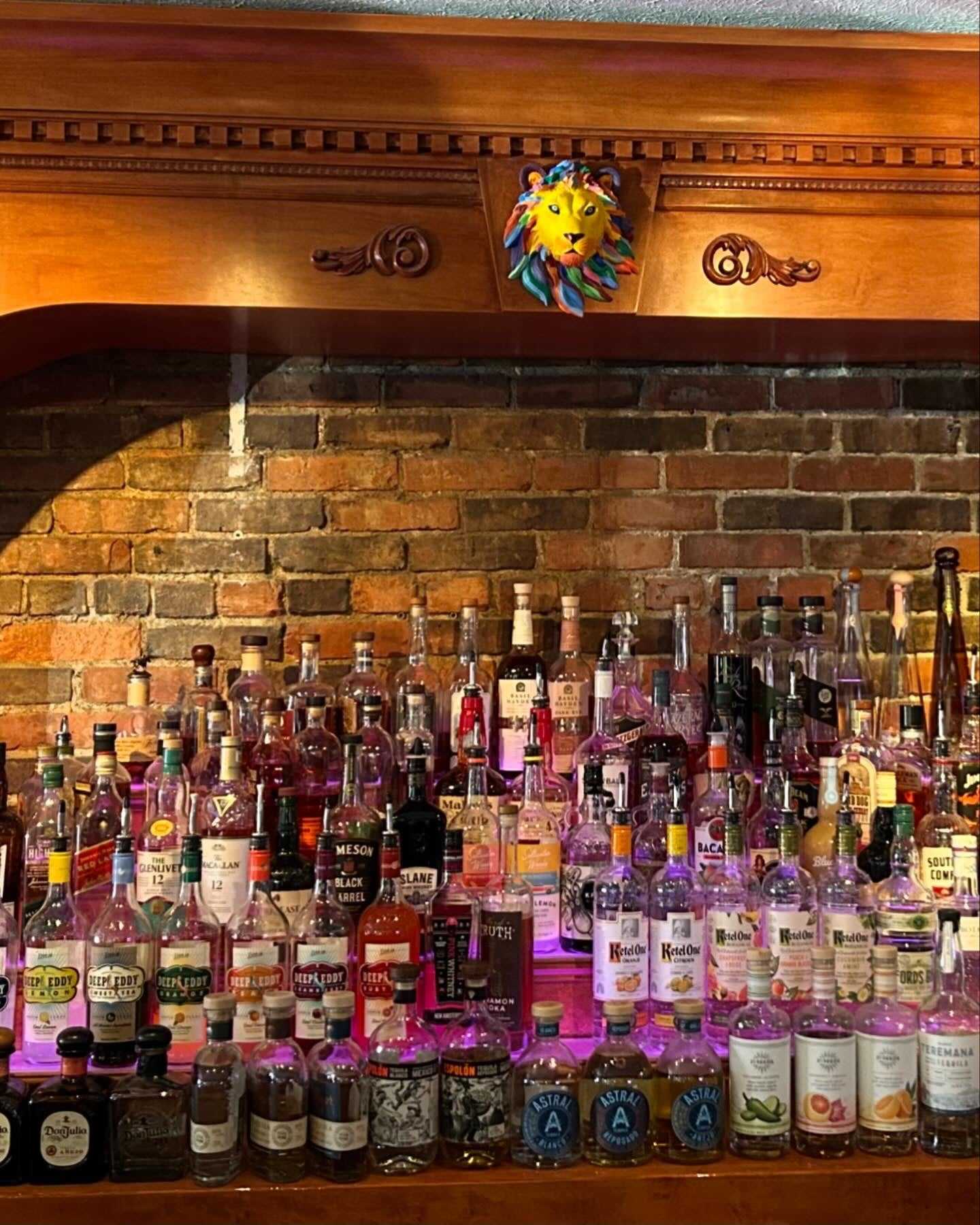 A variety of liquor bottles arranged on a bar shelf with a decorative lion face above.