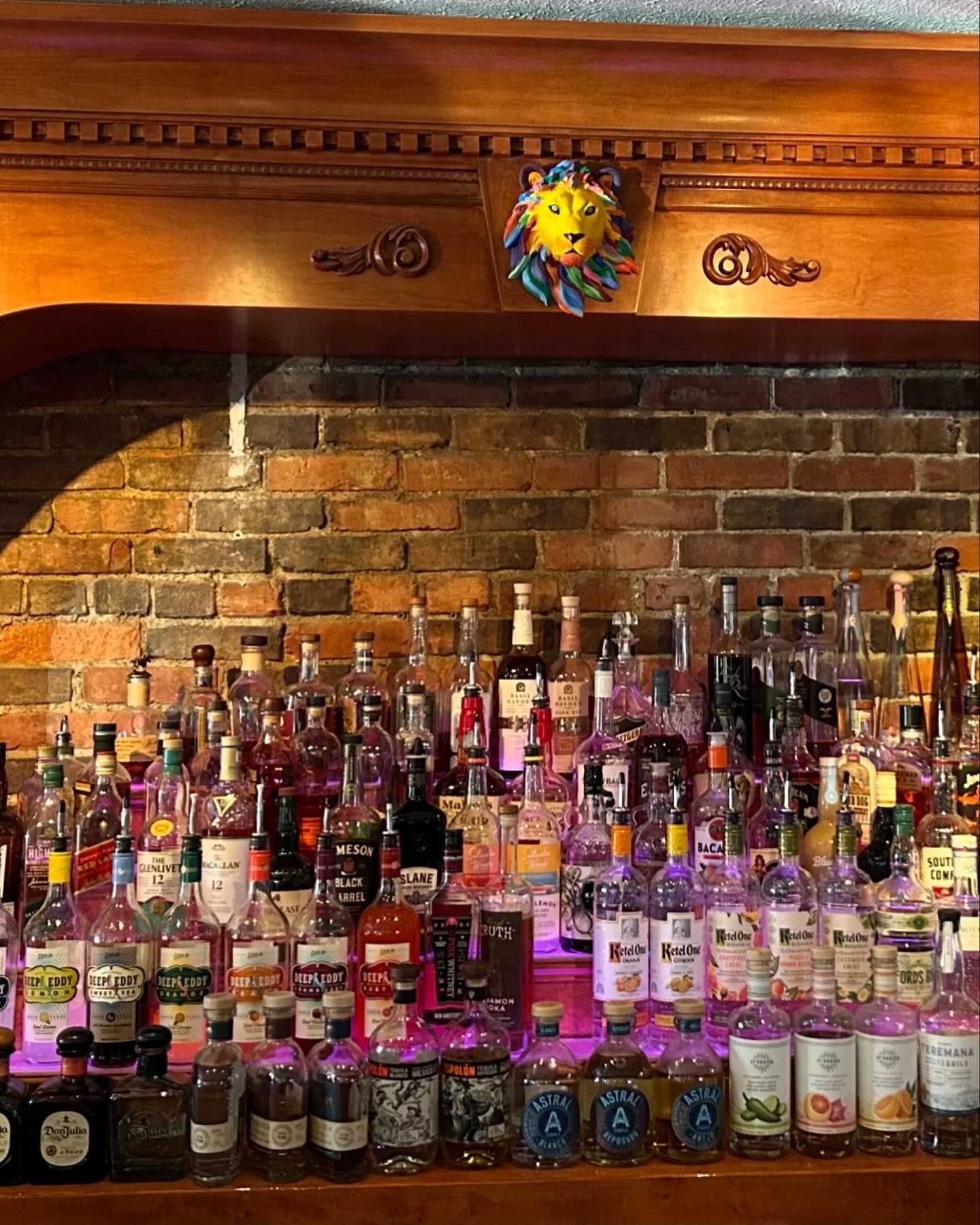 A variety of liquor bottles arranged on a bar shelf with a decorative lion face above.